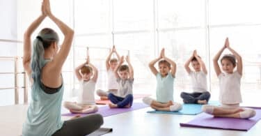 Uma tutora de yoga realizando yoga juntamente a crianças pequenas.