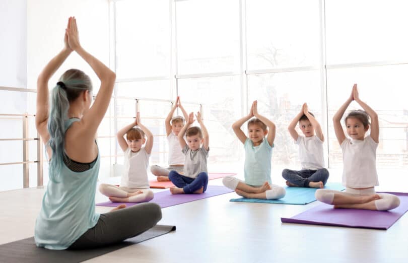 Uma tutora de yoga realizando yoga juntamente a crianças pequenas.