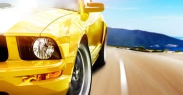 Um mustang amarelo (modelo de carro) percorrendo uma estrada em alta velocidade.