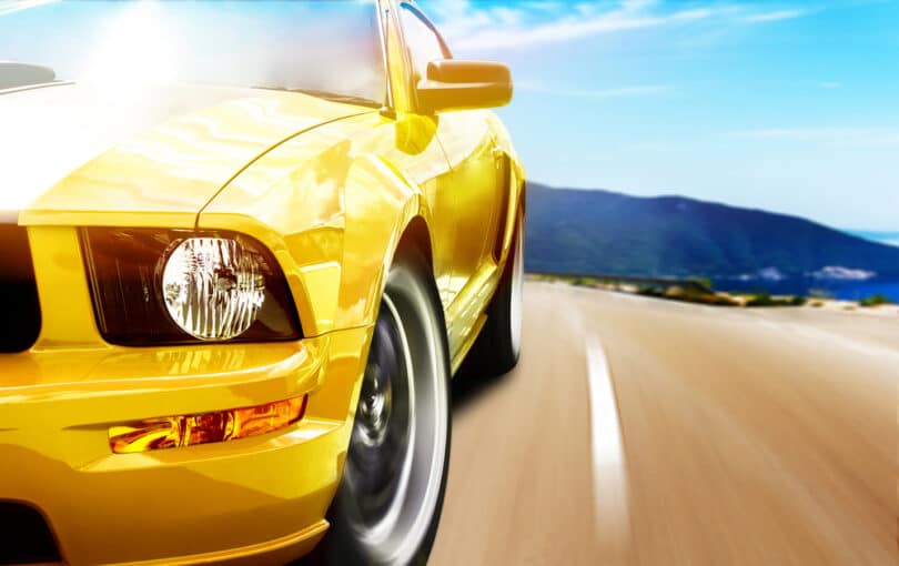 Um mustang amarelo (modelo de carro) percorrendo uma estrada em alta velocidade.