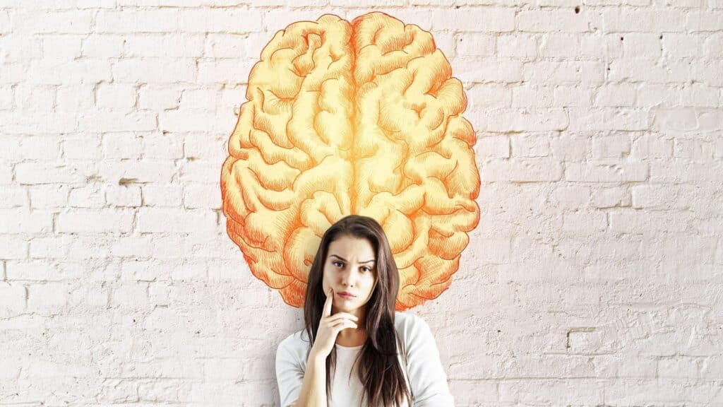 Uma mulher séria. Acima dela, na parede, uma pintura de um cérebro.