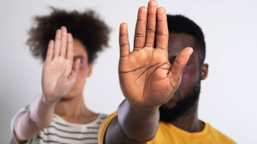 Uma mulher negra e um homem negro realizando, com a mão, um gesto de "pare".