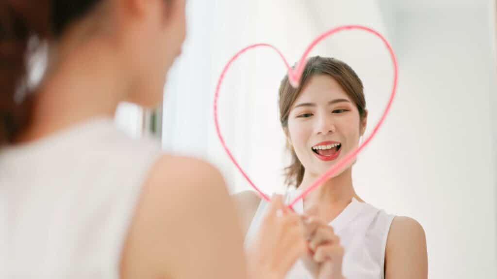Uma mulher sorridente desenhando um coração num espelho.