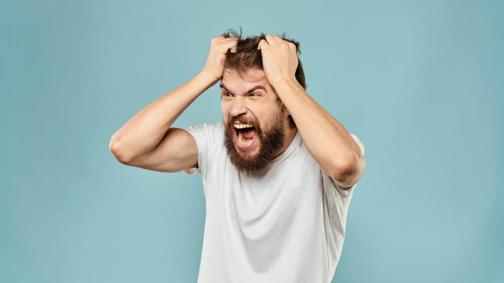 Um homem esbravejando. Ele coloca as suas mãos na sua cabeça.