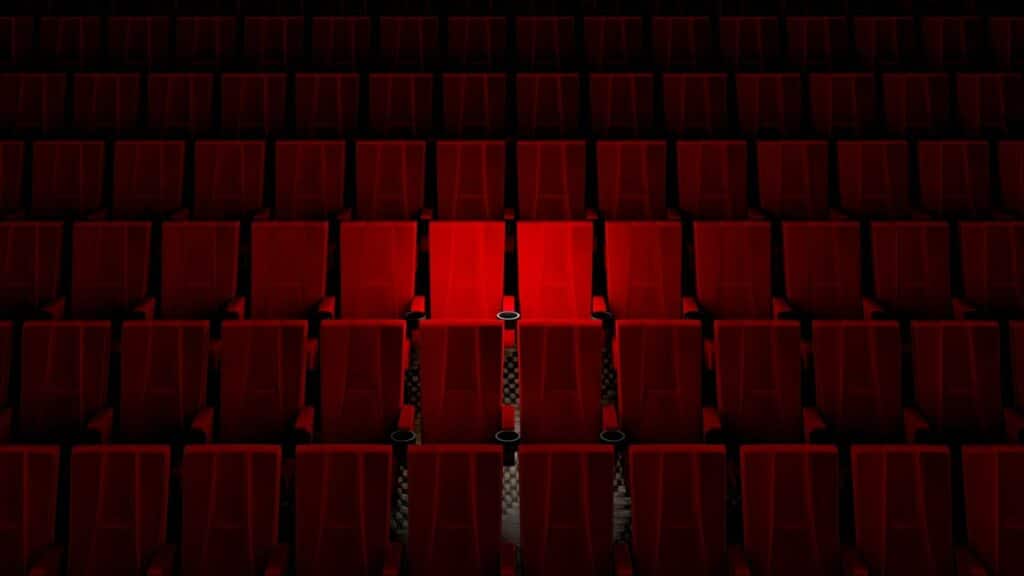 Cadeiras de um palco de teatro. Dentre elas, as do meio, iluminadas, se destacam.