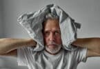 Homem de idade tapando os ouvidos com travesseiro para não ouvir vozes (sintoma de esquizofrenia)