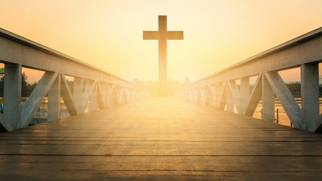 Uma ponte iluminada pelo sol. Ao seu término, uma cruz de madeira.