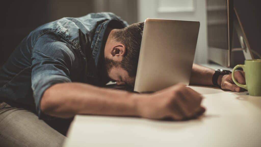Um homem exausto debruçando a sua cabeça no teclado de um notebook.