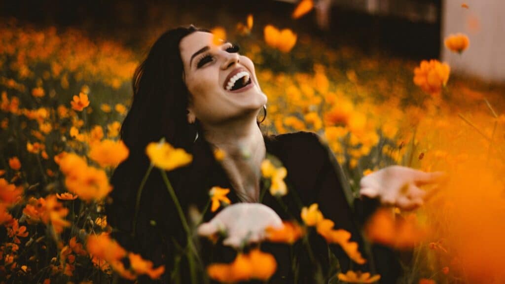 Uma mulher sorrindo. Ela está ao meio de um campo florido.