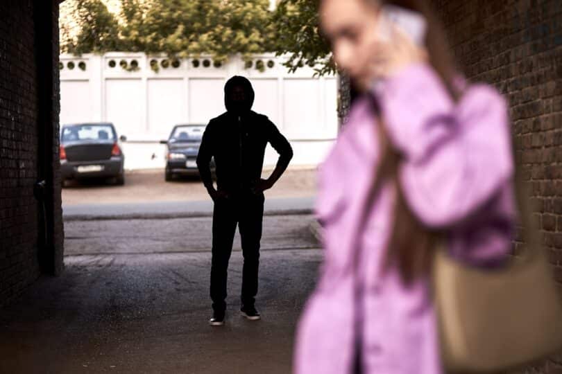 Um stalker de capuz perseguindo uma mulher que fala ao telefone.