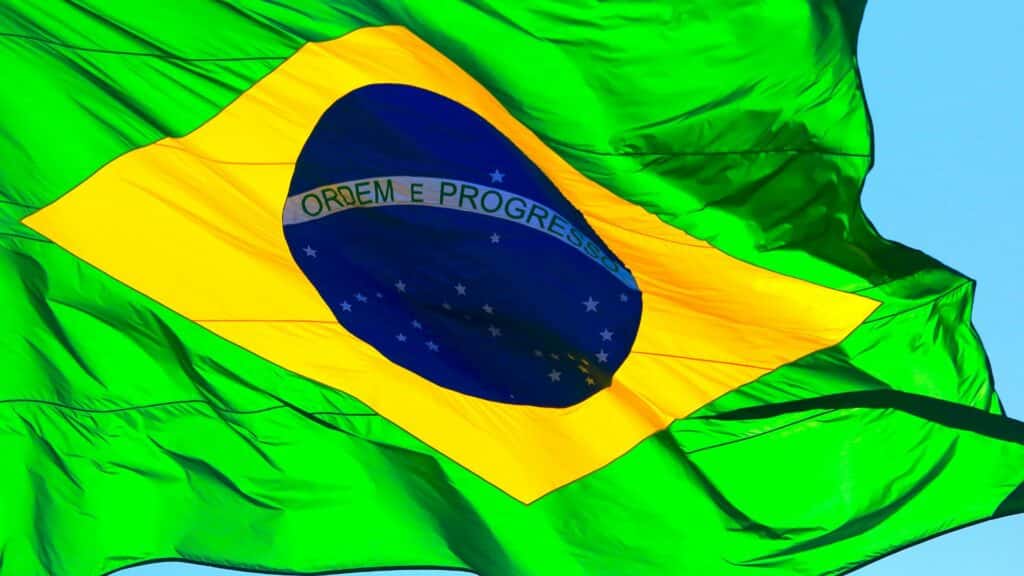 A bandeira do Brasil drapejando. Em destaque, a frase positivista "Ordem e Progresso".