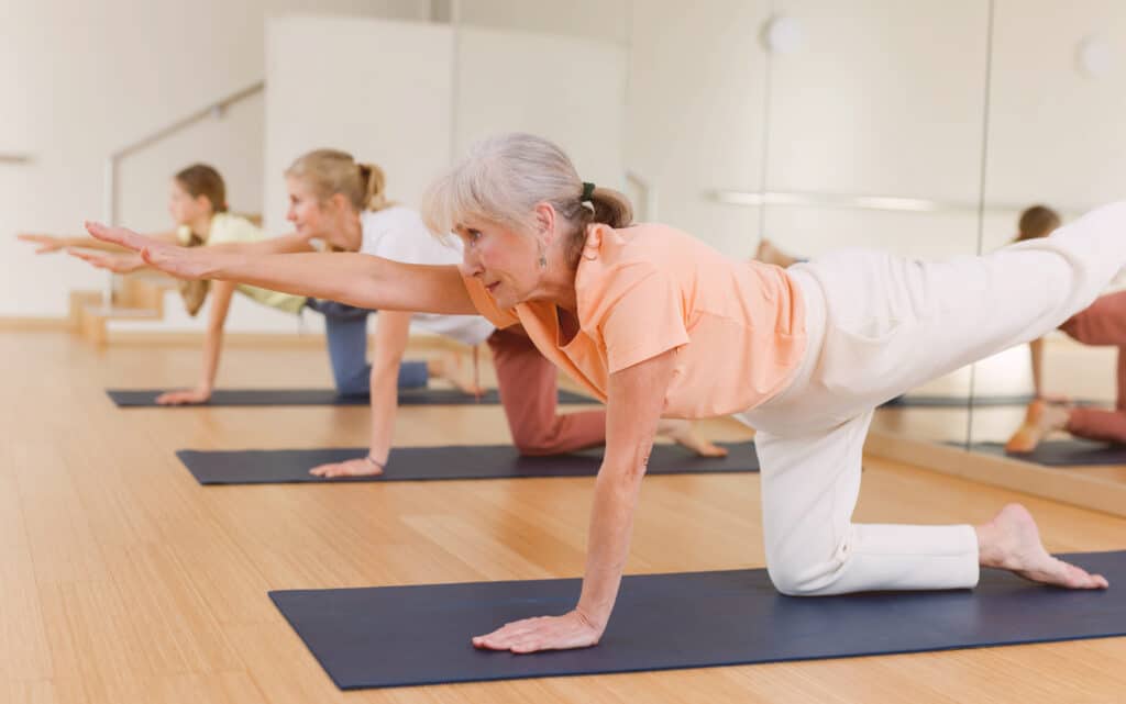 Mulheres de diferentes idades praticando exercício físico sobre seus tapetes.