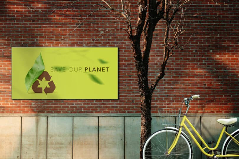 Bicicleta estacionada ao lado de uma árvore aparentemente seca. Ao fundo, na parede, uma placa escrita "Save our planet".