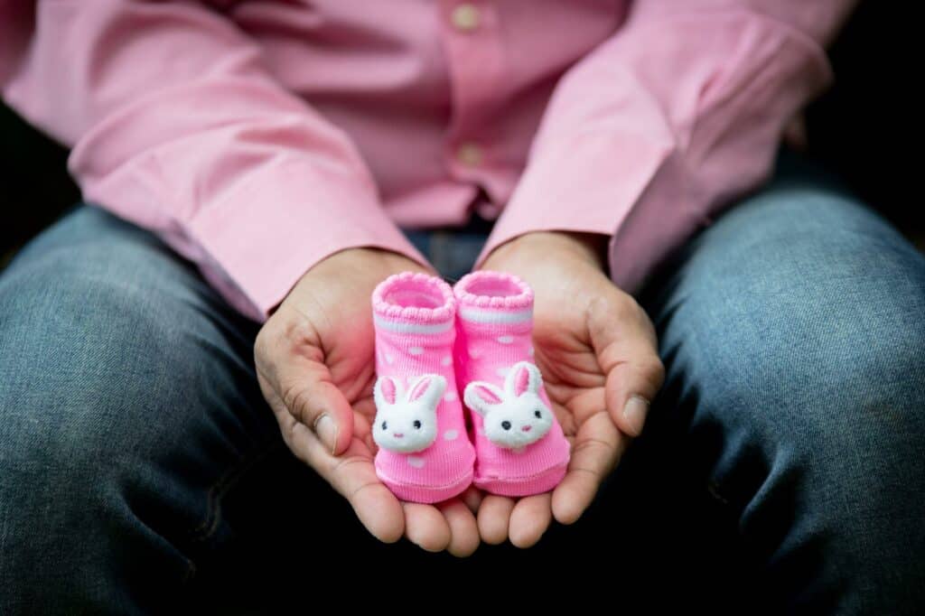 Um sapatinho de bebê rosa está posicionado entre as mãos abertas, em forma de concha.