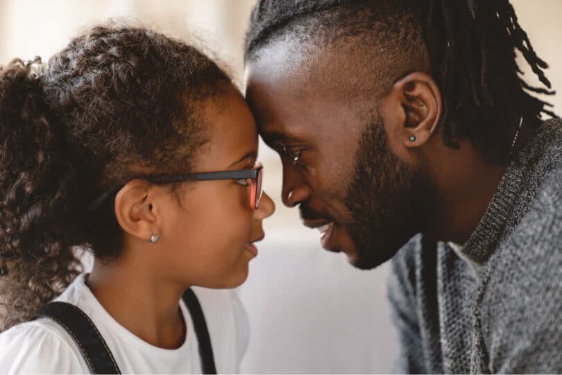 Filha pequena e seu pai com suas testas carinhosamente encostadas.