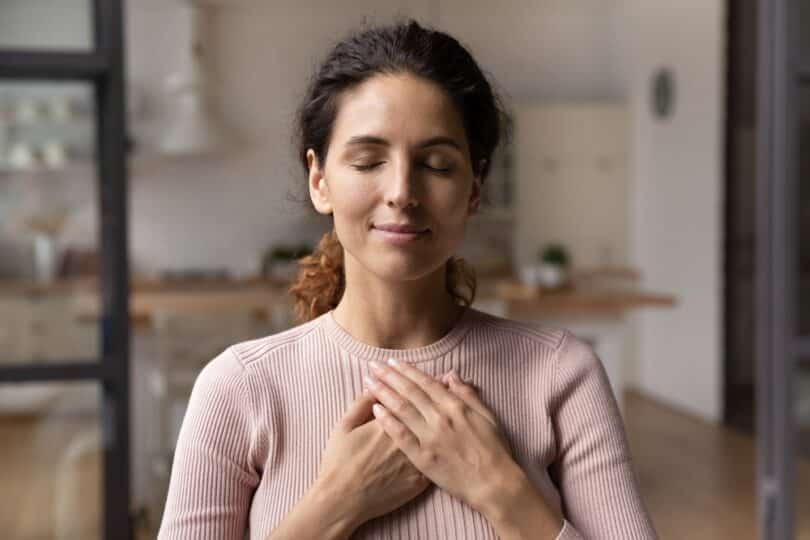 Uma mulher de olhos fechados colocando as suas mãos sobre o peito.