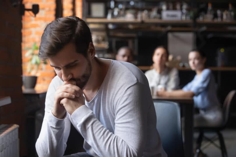 Um homem isolado de um grupo de pessoas. Ele parece triste.