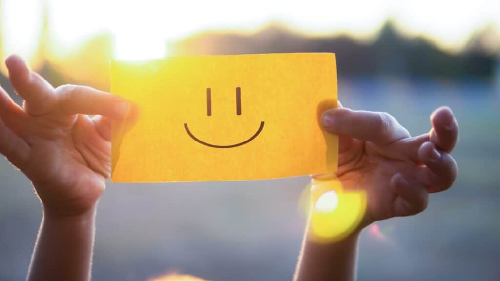 Uma pessoa segurando um papel amarelo que tem o desenho de um sorriso.