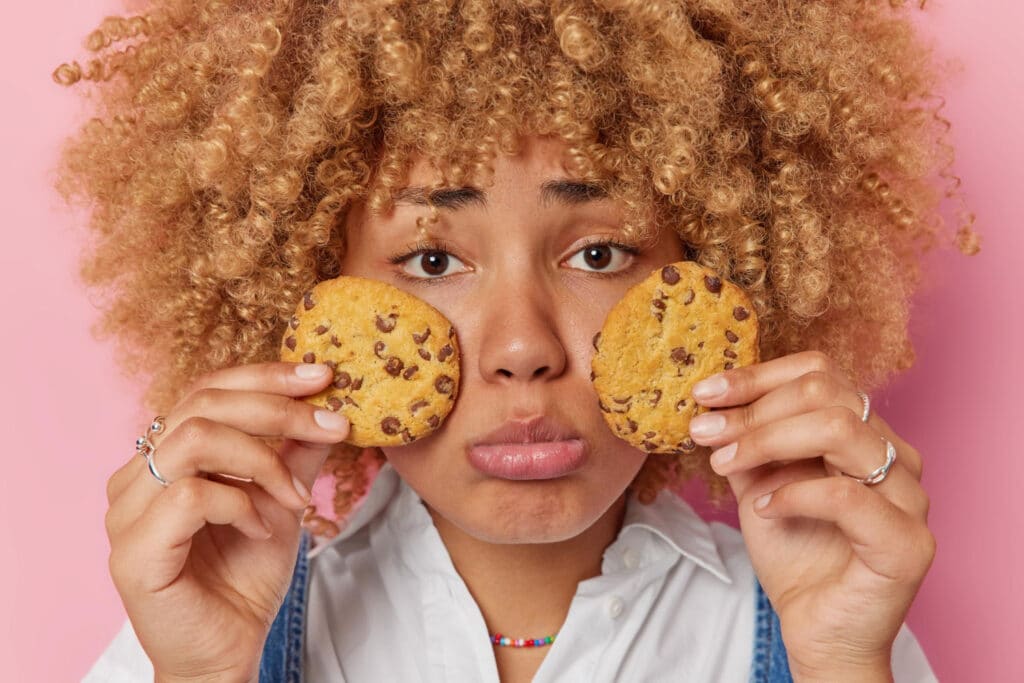 Mulher com expressão triste com dois cookies na mão.