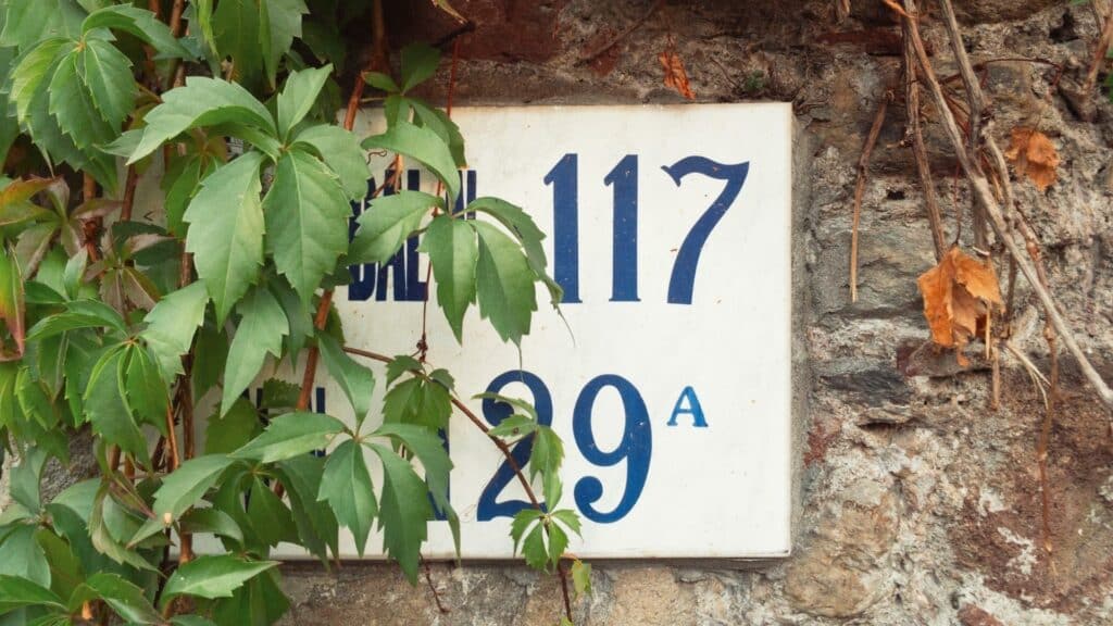Uma placa numérica presa a uma parede. Ela contém os números 117 e 29A.