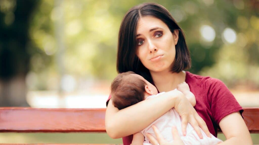Uma mulher com um semblante triste abraçando o seu bebê.