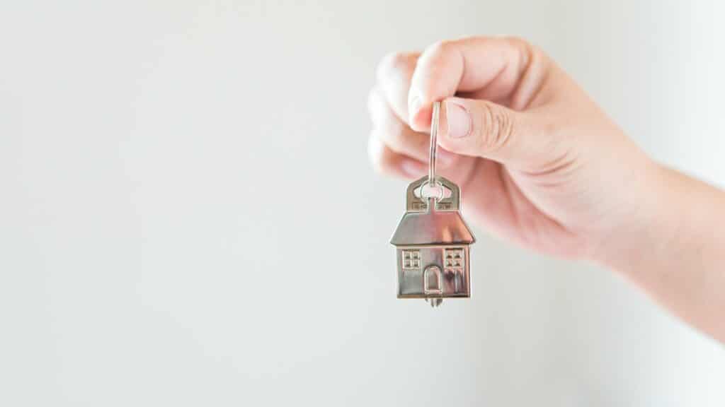 Uma mão segurando uma miniatura de casa construída de metal.