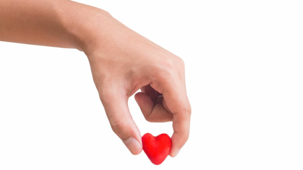 Uma mão segurando uma miniatura de um coração vermelho.