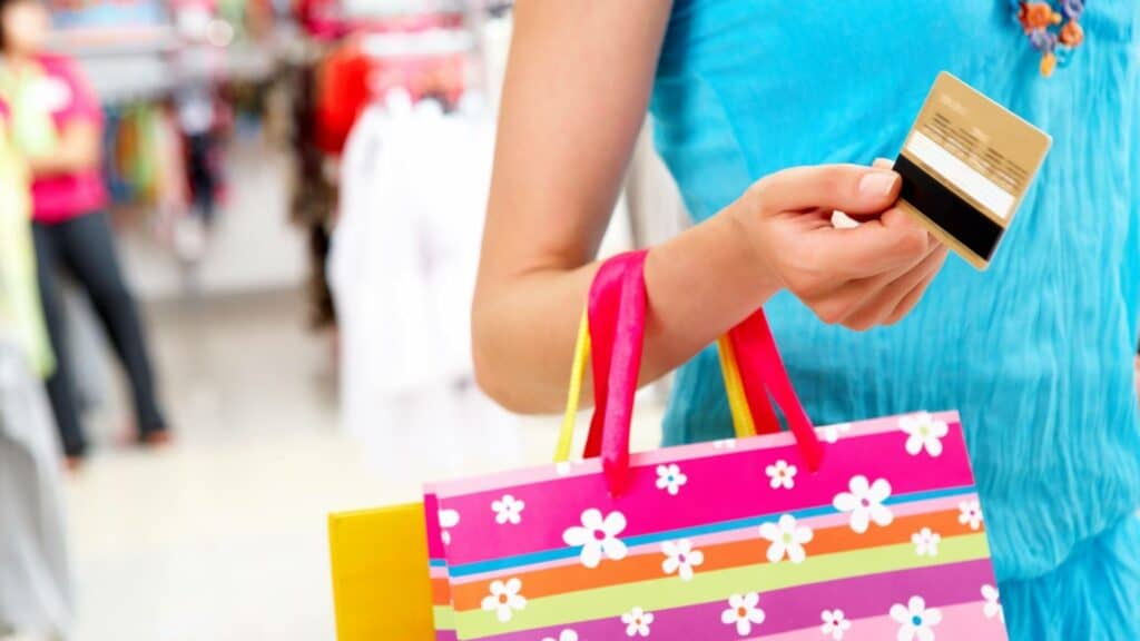 Uma mulher segurando um cartão de crédito e sacolas de compras.