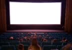 Sala de cinema com alguns espectadores sentados nas cadeiras, aguardando o filme rodar na tela.