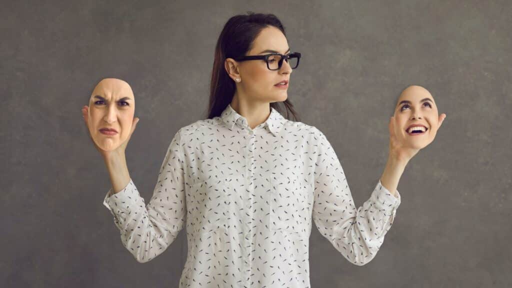 Uma mulher segurando duas ilustrações diferentes de rostos que exibem expressões diferentes.