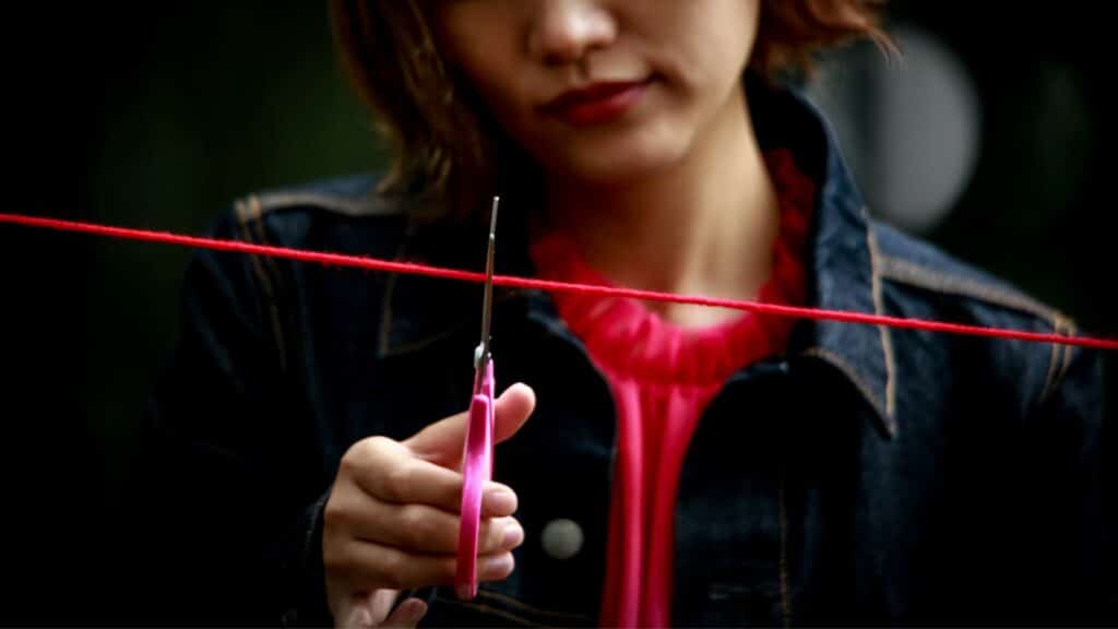 Uma mulher tentando cortar um fio vermelho com uma tesoura rosa.