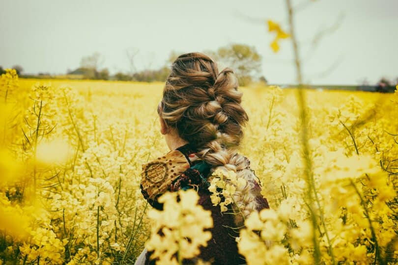Mulher de costas em um campo de flores amarelas.