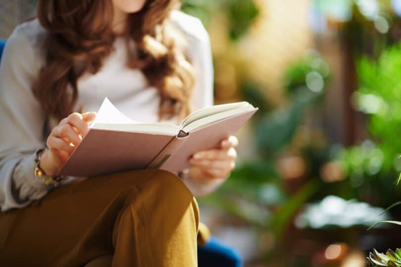 Uma mulher lendo um livro ao ar livre.