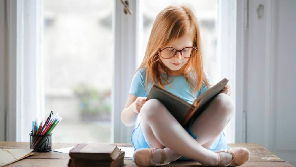 Uma pequena garota lendo um livro à janela.
