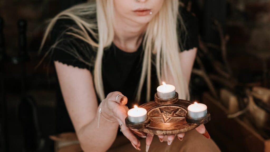 Mulher loira com piercing na boca segurando velas num suporte Wicca