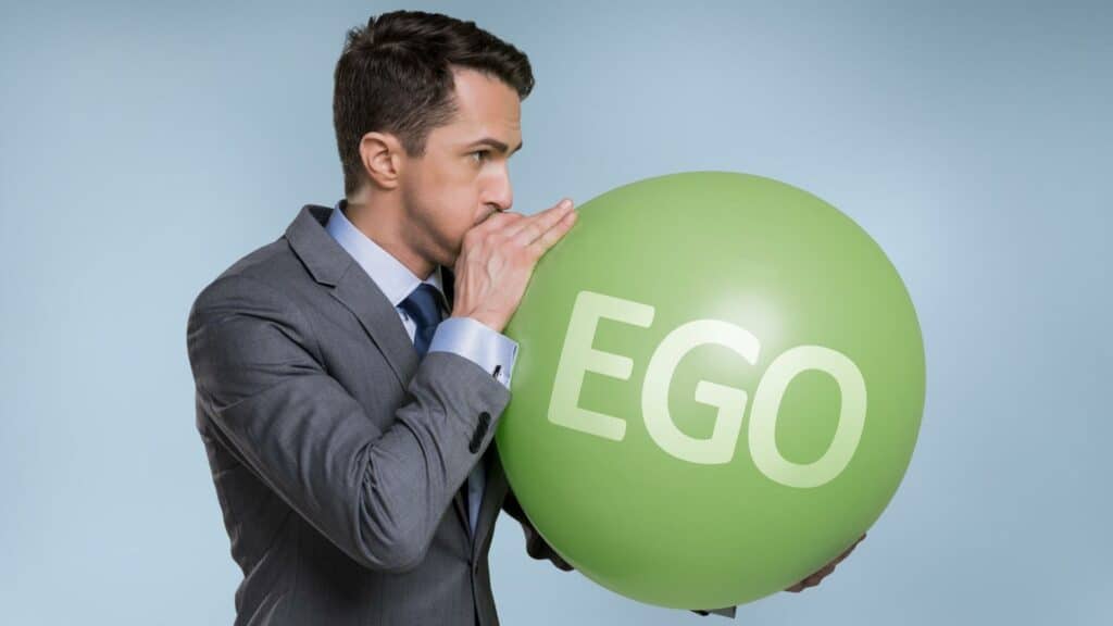Um homem assoprando um balão com a palavra "ego".