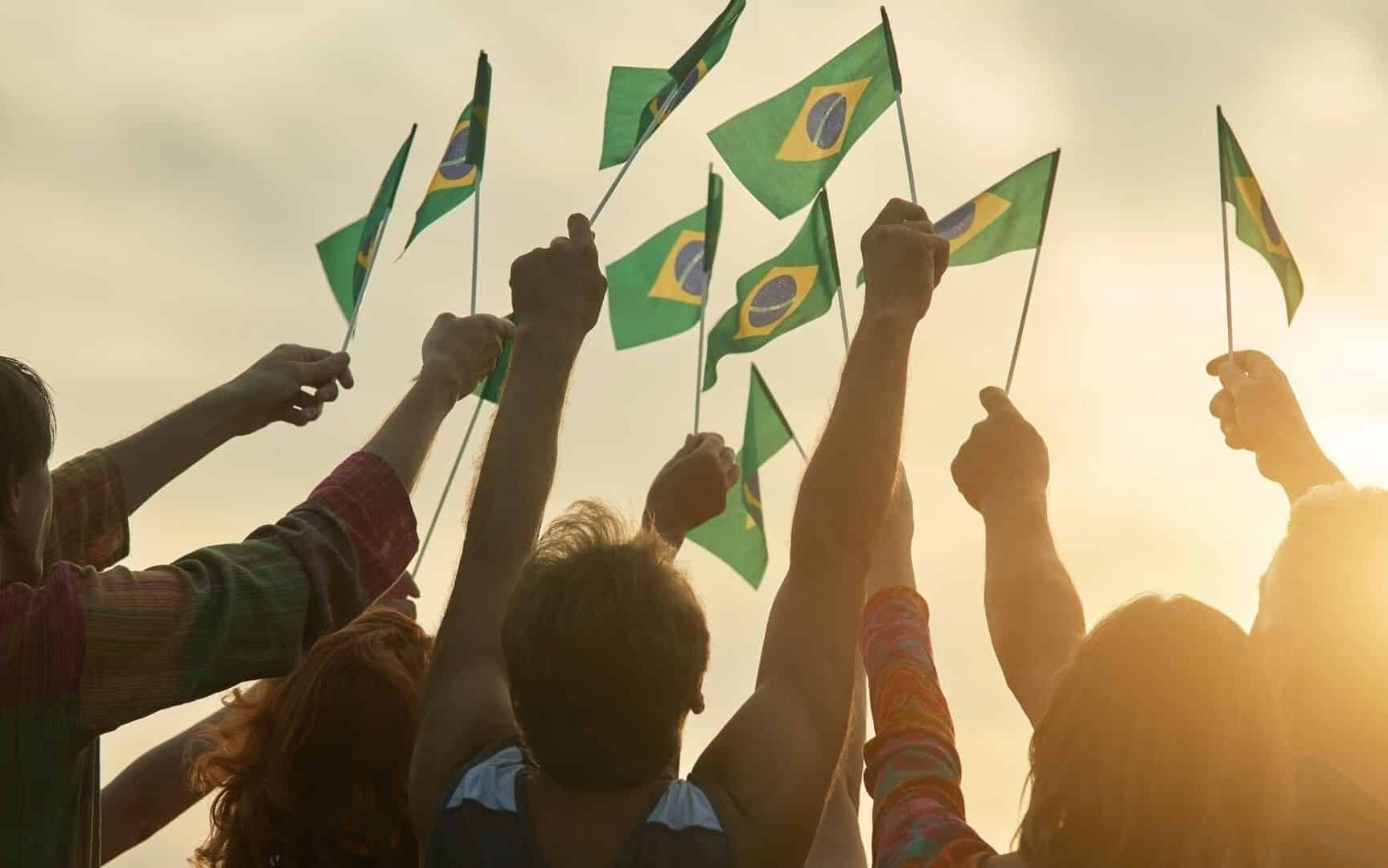 Pessoas erguendo pequenas bandeiras do Brasil.