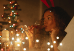 foto de uma mulher tomando uma taça devinho e uma árvore de natal no fundo da imagem