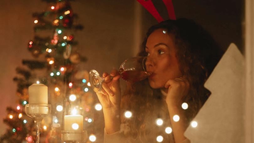 foto de uma mulher tomando uma taça devinho e uma árvore de natal no fundo da imagem