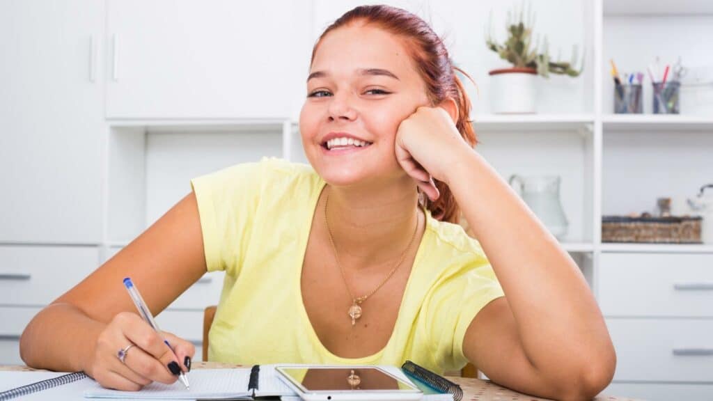 Uma garota realizando anotações num caderno. Ela sorri.