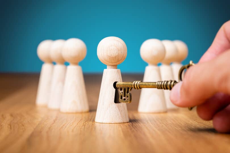 Bonequinhos de maneira sobre a mesa. Em um deles, uma mão masculina introduz uma chave.