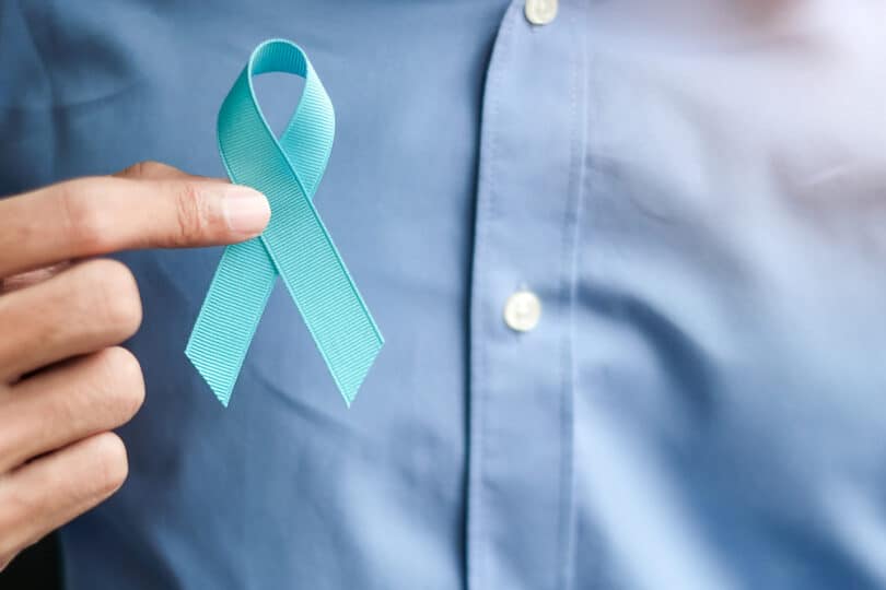 Um homem de camisa social azul segurando a fita azul, que faz alusão ao novembro azul.