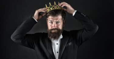 Um homem de terno colocando uma coroa no topo da sua cabeça.