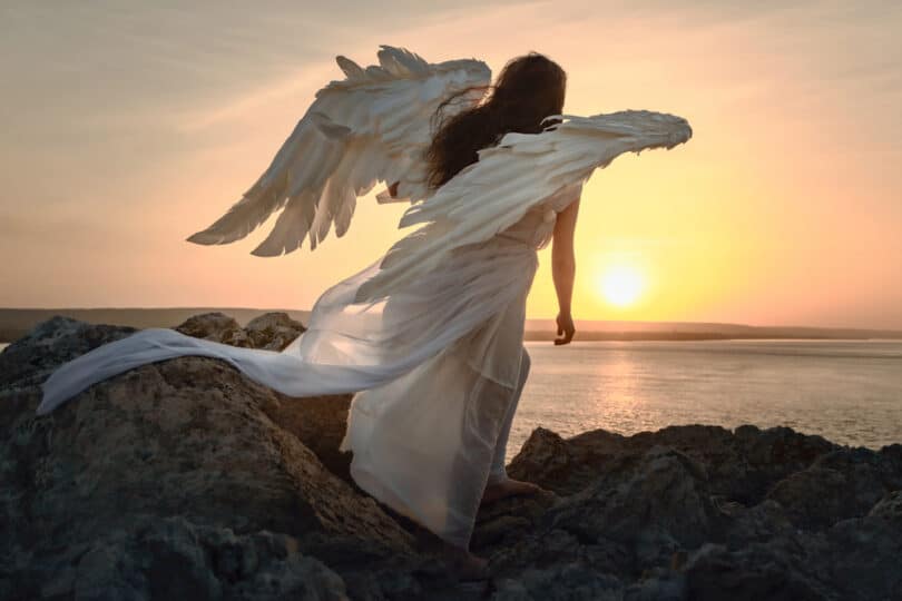 Um anjo à beira de uma praia observando o pôr do sol.