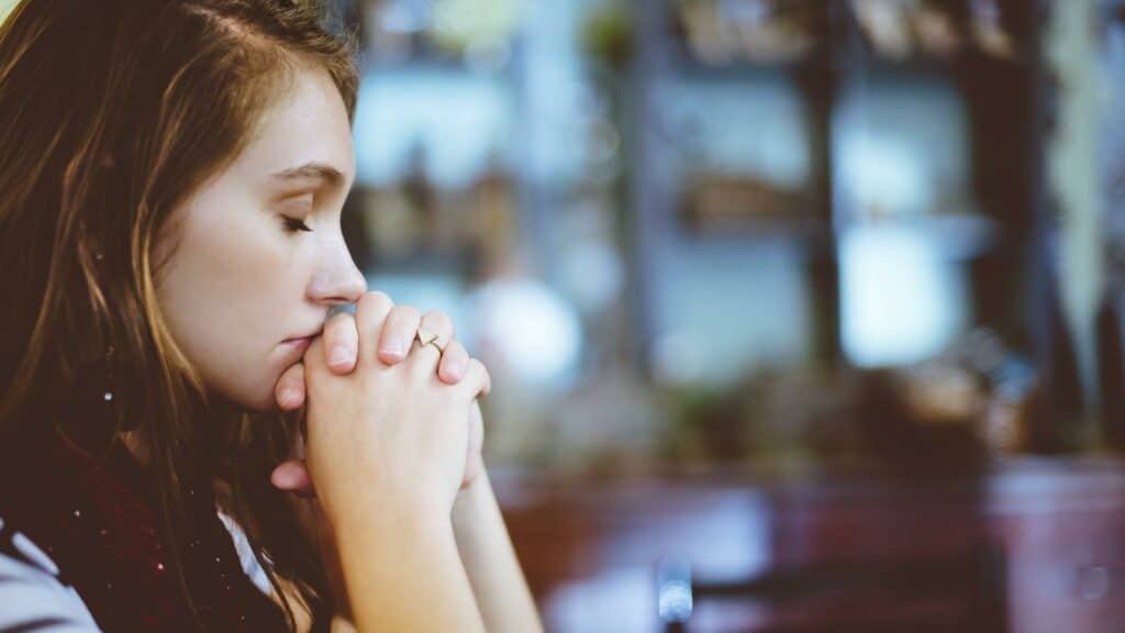 Uma mulher orando de olhos fechados e mãos serradas.