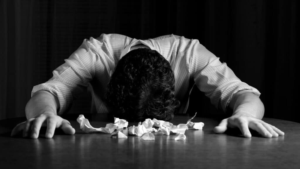 Um homem debruçando seu rosto numa mesa que tem lenços de papel.