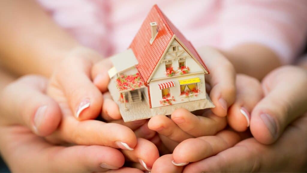 Mãos de uma família segurando uma miniatura de casa.