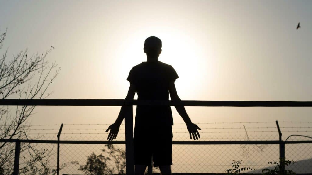 Um homem de braços abertos sendo iluminado pelo sol.