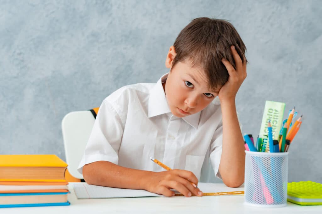 Menino sentado numa mesa escolar, segurando um lápis