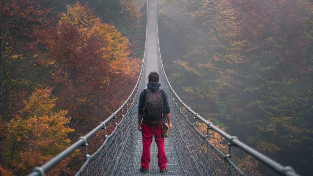 Um homem prestes a atravessar uma ponte instalada sobre uma floresta.